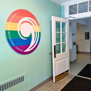 Picture of the rainbow "Comma" sign that hangs in the entry way at Lakewood Congregational Church UCC